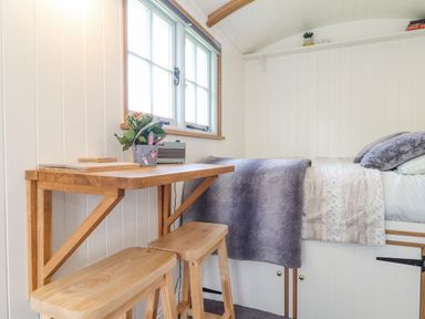 A small wooden table with two stools next to a bed with blankets and pillows at Gwithian Shepherds Hut in Angarrack near Hayle
