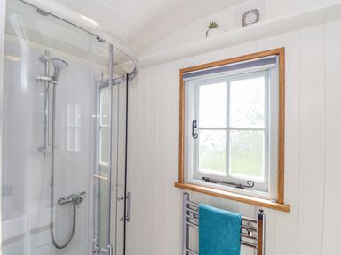A bathroom with a curved glass shower enclosure and a window with frosted glass at Gwithian Shepherds Hut in Angarrack near Hayle