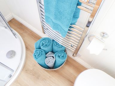 A bathroom corner with rolled blue and gray towels in a basket beside a chrome towel rack and toilet paper holder at Gwithian Shepherds Hut in Angarrack near Hayle