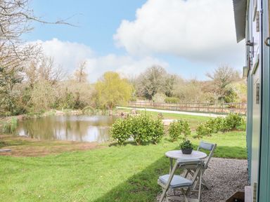 A garden with a small pond shrubs and two chairs with a table outside a building at Gwithian Shepherds Hut in Angarrack near Hayle