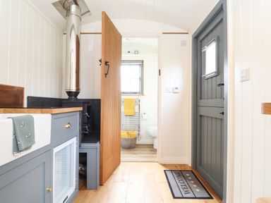A small kitchen area with a wood stove and a door leading to a bathroom at Godrevy Shepherds Hut in Angarrack near Hayle