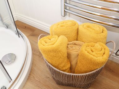 A basket with rolled yellow towels next to a shower and heated towel rail in a bathroom at Godrevy Shepherds Hut Angarrack near Hayle