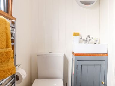 A small bathroom with a toilet a sink on a blue cabinet and yellow towels at Godrevy Shepherds Hut Angarrack near Hayle