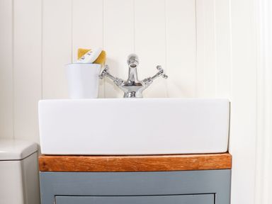 A bathroom sink with a chrome faucet a white container holding a yellow cloth and a tube next to a toilet at Godrevy Shepherds Hut in Angarrack near Hayle