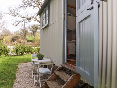 An outdoor table with two chairs and potted plants next to a shepherds hut with open half door at Godrevy Shepherds Hut Angarrack near Hayle
