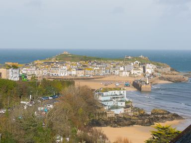 A coastal town with houses on a hill overlooking a beach with boats and a pier at Godrevy Shepherds Hut in Angarrack near Hayle