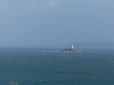 A lighthouse on a rocky island in the sea with cliffs in the background at Godrevy Shepherds Hut Angarrack near Hayle