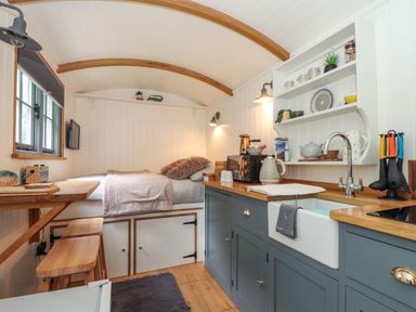 A compact kitchen and sleeping area with a countertop sink and wooden stools at Godrevy Shepherds Hut in Angarrack near Hayle