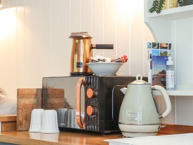 A kitchen counter with a microwave, electric kettle, coffee pot, mugs, and informational books at Godrevy Shepherds Hut in Angarrack near Hayle