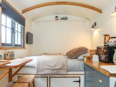 A small room with a bed table stools and kitchen appliances at Godrevy Shepherds Hut in Angarrack near Hayle