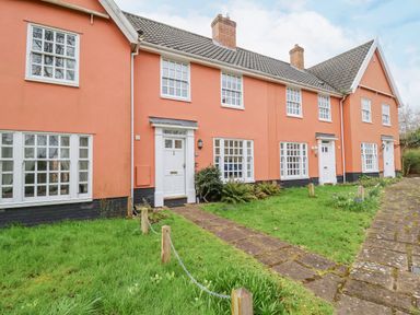 A row of orange townhouses with white doors and windows and green lawns in front at 23 Church Farm Lane in Halesworth