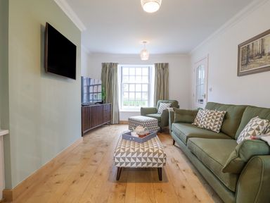 A living room with green sofa and armchair wooden floor and wall mounted tv at 23 Church Farm Lane in Halesworth