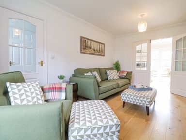 A living room with green sofas patterned ottomans wooden floor and a painting on the wall at 23 Church Farm Lane in Halesworth