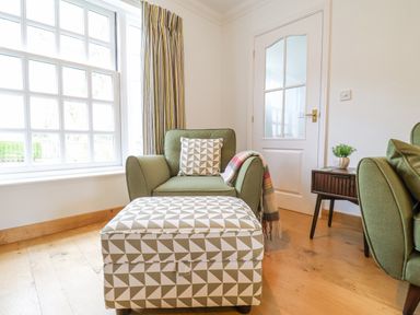 A green armchair with a patterned cushion and matching ottoman next to a wooden side table with a plant at 23 Church Farm Lane in Halesworth