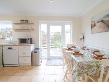 A kitchen and dining area with a table set for six and glass doors leading to a garden at 23 Church Farm Lane in Halesworth