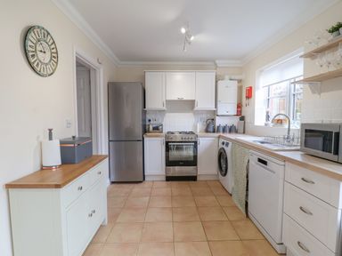 A kitchen with white cabinets a refrigerator a washing machine a dishwasher and a microwave at 23 Church Farm Lane in Halesworth