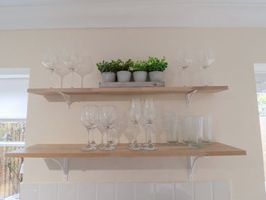 Two wooden wall shelves with glassware and potted plants in a kitchen at 23 Church Farm Lane in Halesworth