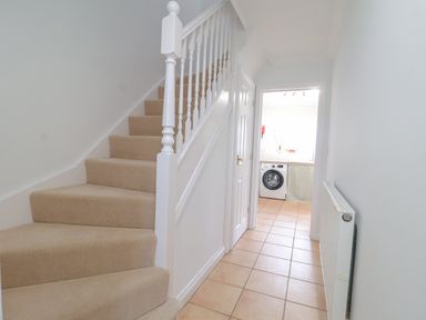 A hallway with tiled floor and carpeted stairs leading up to the left with a doorway to a laundry room at 23 Church Farm Lane in Halesworth