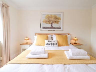 A bedroom with a bed featuring yellow pillows and a cushion saying lets snuggle at 23 Church Farm Lane in Halesworth