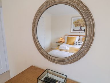 A round wall mirror reflecting a bedroom with a bed pillows and a bedside lamp at 23 Church Farm Lane in Halesworth