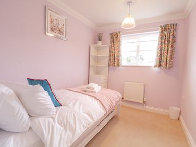 A small bedroom with a single bed white shelves a window with floral curtains and a wall radiator at 23 Church Farm Lane in Halesworth