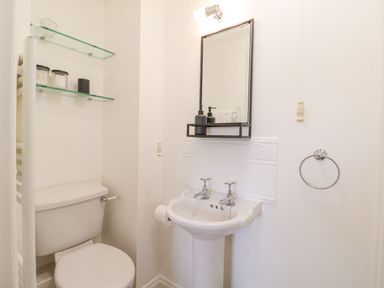 A bathroom with a toilet, pedestal sink, mirror with shelf, and glass shelves on the wall at 23 Church Farm Lane in Halesworth