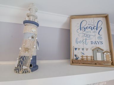 A decorative lighthouse model and a framed beach themed sign on a white shelf at 23 Church Farm Lane in Halesworth