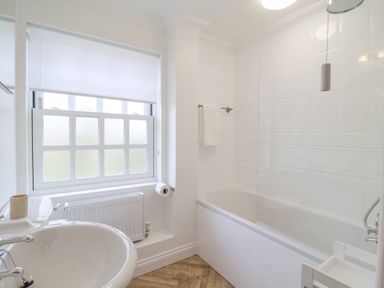 A bathroom with a sink a bathtub a window with a blind and a towel on a rail at 23 Church Farm Lane in Halesworth