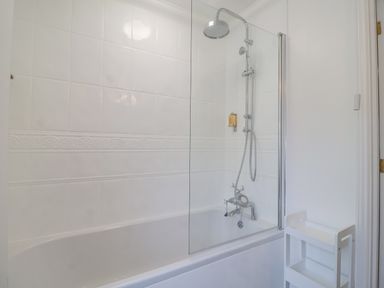 A bathroom with a bathtub shower combination with glass panel and a white storage rack at 23 Church Farm Lane in Halesworth