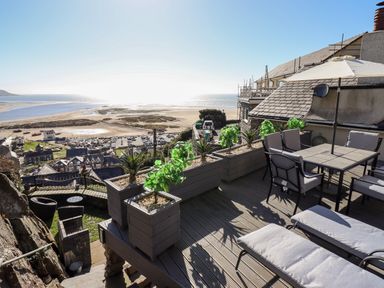 A terrace with outdoor seating and plants overlooking a beach and town at Ty'n-Y-Ffynnon Cottage in Barmouth