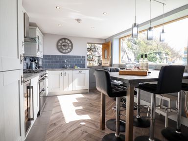 A kitchen with white cabinets a wooden table black chairs and a large window at Ty'n-Y-Ffynnon Cottage in Barmouth