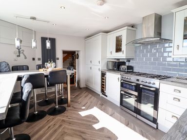 A kitchen with white cabinets black bar stools and a gas stove at Ty'n-Y-Ffynnon Cottage in Barmouth