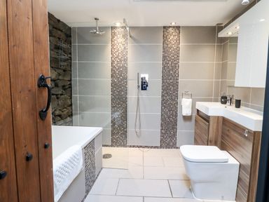 A bathroom with a bathtub a walk in shower a toilet and a sink with wooden cabinets at Ty'n-Y-Ffynnon Cottage in Barmouth