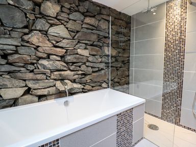 A bathroom with a bathtub and a shower area with stone and tile walls at Ty'n-Y-Ffynnon Cottage in Barmouth