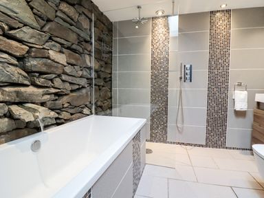 A bathroom with a bathtub and stone and tile walls at Ty'n-Y-Ffynnon Cottage in Barmouth