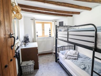 A bedroom with bunk beds a chest of drawers a wooden door and a window at Ty'n-Y-Ffynnon Cottage in Barmouth