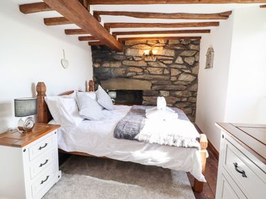 A bedroom with a wooden bed and a stone wall at Ty'n-Y-Ffynnon Cottage in Barmouth