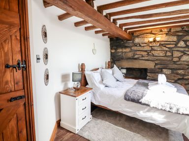 A bedroom with a bed pillows bedside table lamp and exposed wooden beams at Ty'n-Y-Ffynnon Cottage in Barmouth