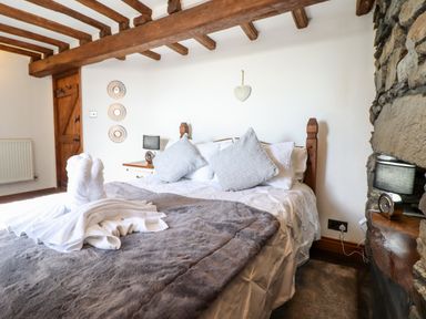 A bedroom with a wooden bed frame gray pillows and a gray blanket with exposed wooden beams and stone wall at Ty'n-Y-Ffynnon Cottage in Barmouth