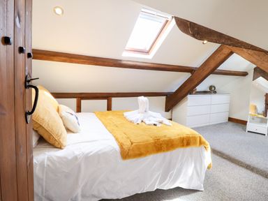 A bedroom with a bed covered in white and yellow bedding under a skylight with wooden beams at Ty'n-Y-Ffynnon Cottage in Barmouth