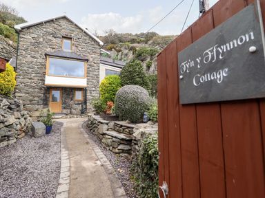 A stone cottage with a pathway and garden behind a wooden gate at Ty'n-Y-Ffynnon Cottage in Barmouth