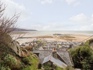 Sea view over rooftops and sandy beach with hills in the background at Ty'n-Y-Ffynnon Cottage in Barmouth