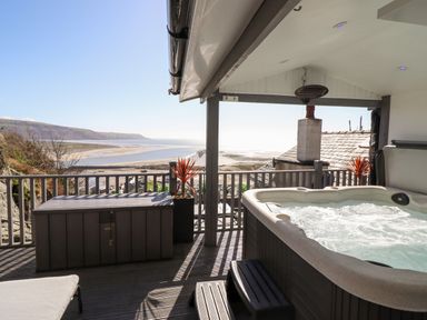 A covered patio with a hot tub and a storage box overlooking a beach and hills at Ty'n-Y-Ffynnon Cottage in Barmouth