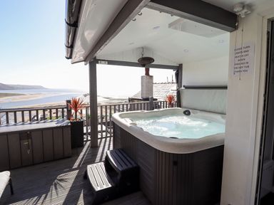 An outdoor covered deck with a hot tub steps and a view of a beach at Ty'n-Y-Ffynnon Cottage in Barmouth