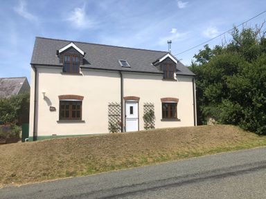 A two-story house with a white door and windows next to a road at Ty Rhosyn Penycwm near Solva