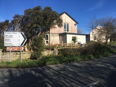A roadside scene with a directional sign and houses with trees and flowers at Ty Rhosyn in Penycwm near Solva