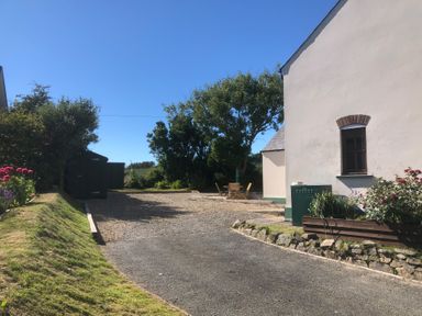A driveway with gravel and a seating area beside a white building with plants at Ty Rhosyn in Penycwm near Solva