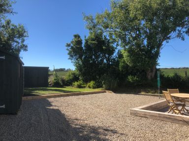 A garden area with gravel ground wooden sheds and wooden chairs and table surrounded by trees and grass at Ty Rhosyn in Penycwm near Solva