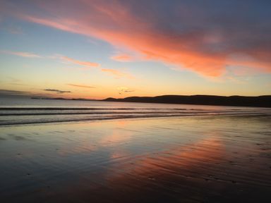 A beach with calm waves and a colorful sky during sunset at Ty Rhosyn Penycwm near Solva