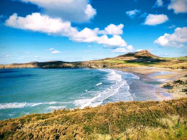 A coastal landscape with a sandy beach waves and a hill in the background at Ty Rhosyn in Penycwm near Solva